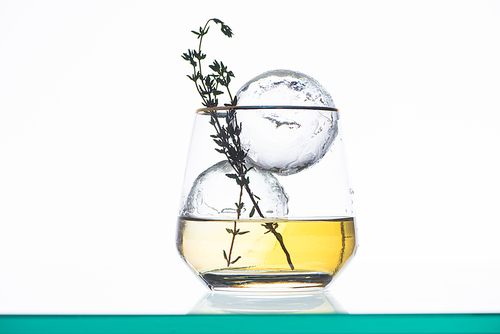 transparent glass with golden liquid, herb and round ice isolated on white