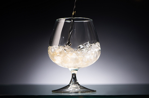 whiskey pouring into transparent glass with ice in dark with back light