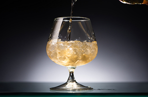 whiskey pouring into transparent glass with ice in dark with back light