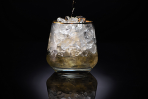 transparent glass with ice and pouring golden liquid on black background