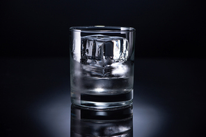 transparent glass with ice cube and vodka on black background