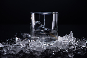 transparent glass with vodka and blueberries near smashed ice isolated on black