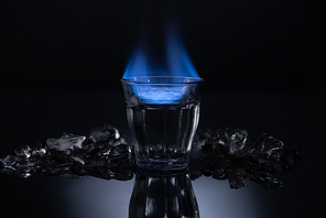 transparent glass with burning liquid near ice on black background