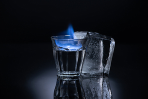 transparent glass with burning liquid near ice on black background
