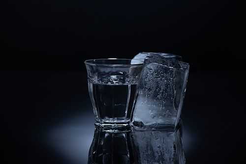 transparent glass with ice cube and vodka on black background
