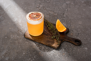 cocktail with orange and herb on wooden cutting board on concrete surface