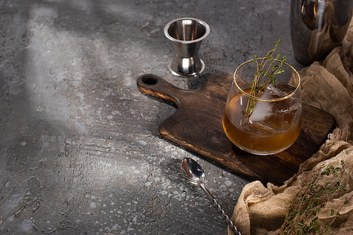 transparent glass with herb, ice cube and whiskey on concrete surface with bar equipment