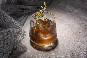 transparent glass with herb, ice cube and whiskey on concrete surface with mesh cloth