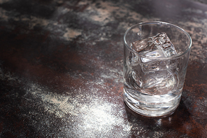 transparent glass with ice cube and vodka on weathered surface