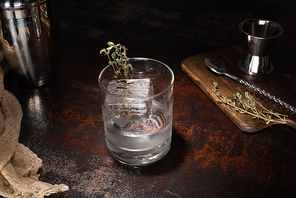 transparent glass with herb, ice cube and vodka on weathered surface