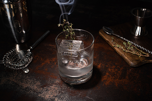 transparent glass with burning herb, ice cube and vodka on weathered surface