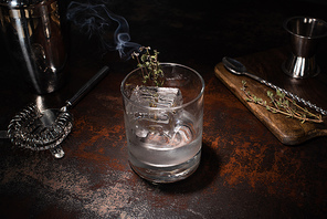 transparent glass with burning herb, ice cube and vodka on weathered surface