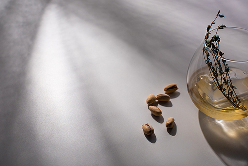transparent glass with herb, ice cube and whiskey on white table with shadow near pistachios