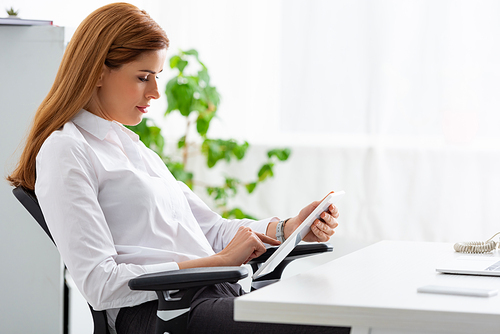 Side view of businesswoman using digital tablet at table in office