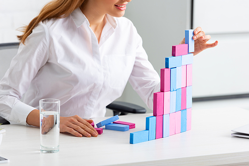 Cropped view of smiling businesswoman stacking marketing pyramid from building blocks on table