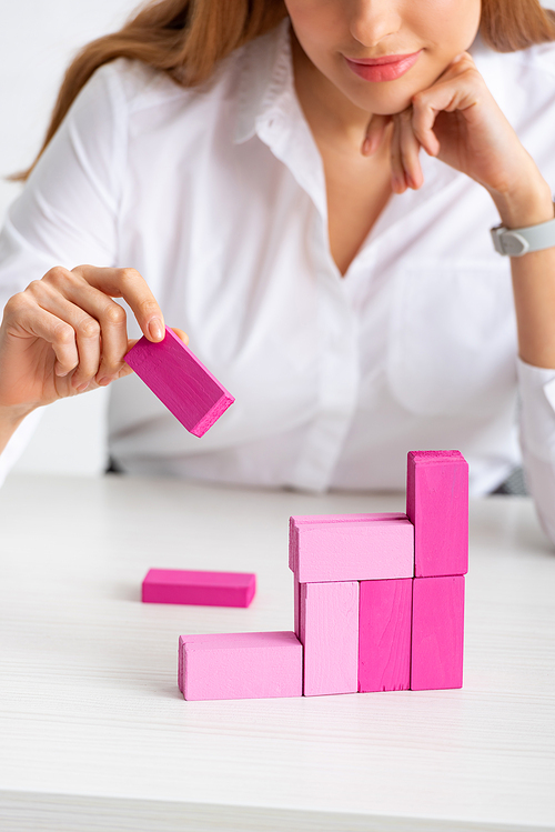 Selective focus of businesswoman stacking marketing pyramid with pink building blocks isolated on grey