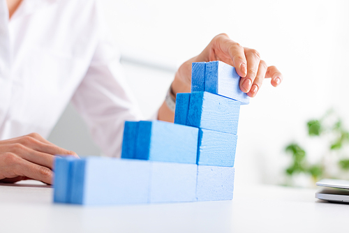 Selective focus of businesswoman making marketing pyramid with blue building blocks near laptop on table