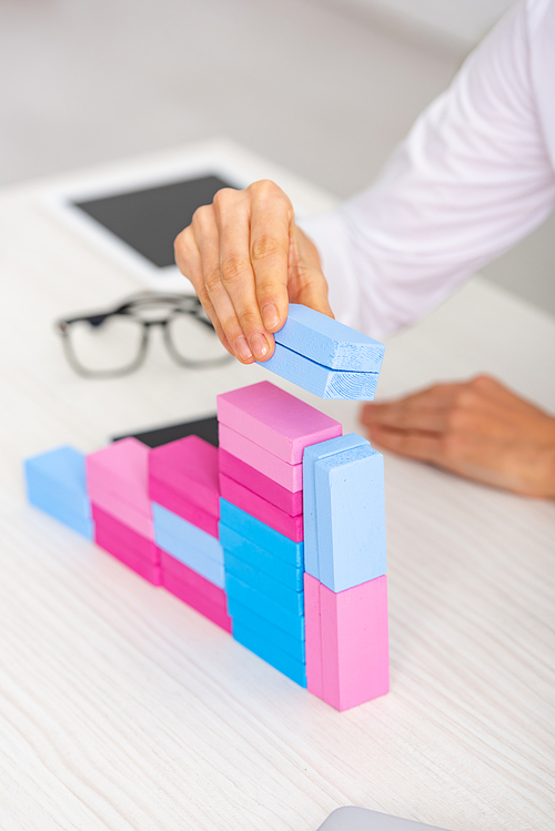 Cropped view of businesswoman making marketing pyramid from colorful building blocks on table