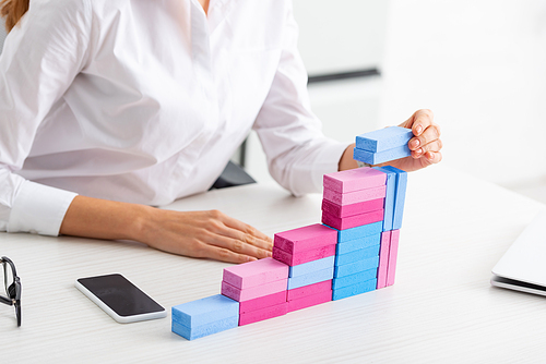 Cropped view of businesswoman stacking marketing pyramid from building blocks on table