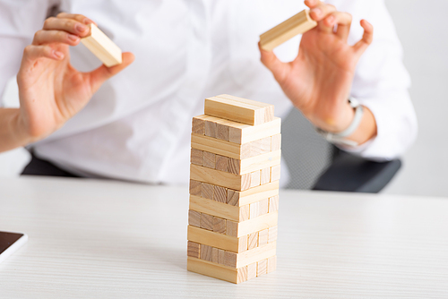 Cropped view of businesswoman stacking wooden building blocks on table on grey background