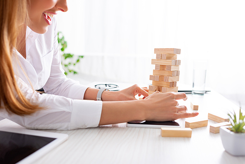 Cropped view of smiling businesswoman stacking wooden building blocks on table