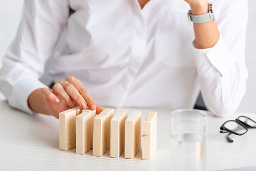 Selective focus of businesswoman stacking wooden building blocks near eyeglasses and glass of water on table isolated on grey