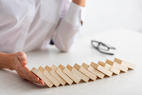 Cropped view of businesswoman holding falling building blocks on table on white background