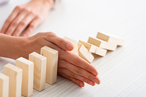 Cropped with of businesswoman holding falling building blocks with hand on table on white background