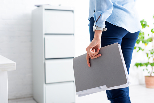 Cropped view of businesswoman holding folder with dossier in office