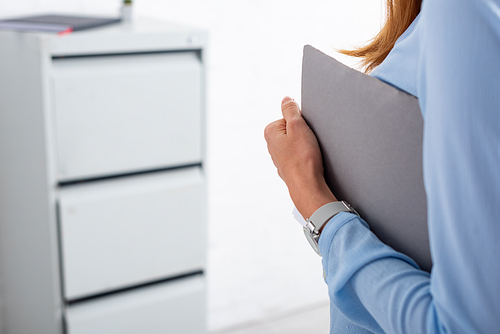 Cropped view of businesswoman holding paper folder in office