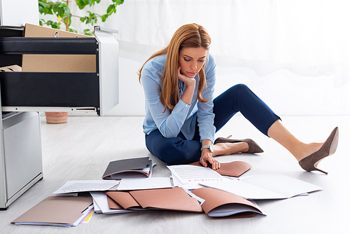 Attractive businesswoman looking at contract and documents near open cabinet driver on floor