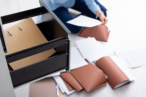Selective focus of businesswoman with documents near open cabinet driver sitting on floor