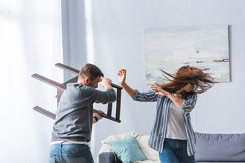 Abusive man holding chair near screaming wife at home