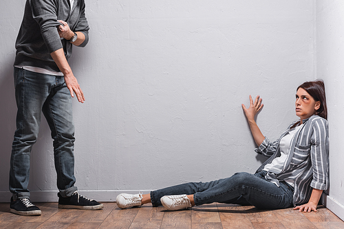 Scared woman with bruises sitting on floor near abuser rolling up sleeves