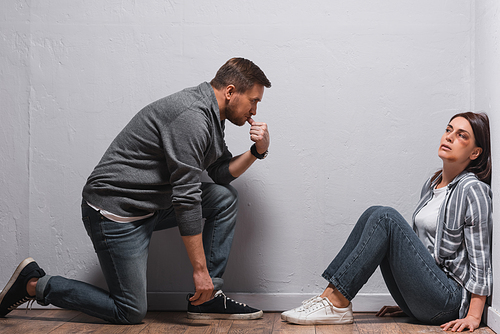 Scared woman with bruises on face looking at pensive abusive husband on floor