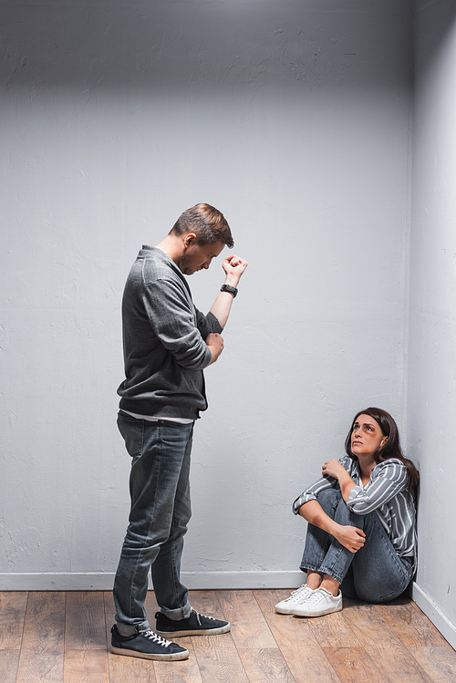 Abusive husband showing fist to scared wife in bruises on floor