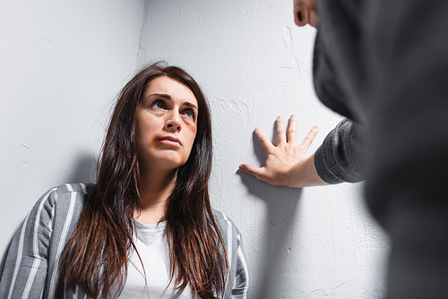 Woman with bruises on face looking at abuser on blurred foreground near walls