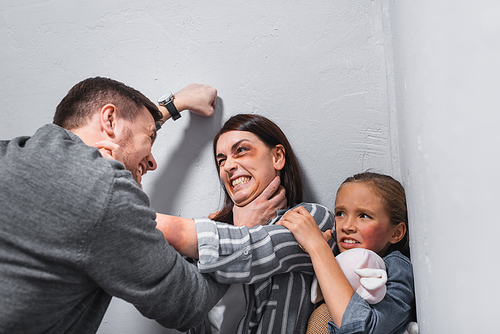 Angry man choking wife with bruises near daughter with soft toy