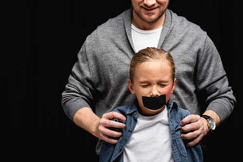 Smiling abused hugging daughter with adhesive tape and bruise isolated on black