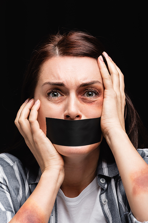 Portrait of woman with bruises and adhesive tape on mouth isolated on black