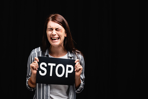 Crying victim of domestic abuse holding card with stop lettering isolated on black