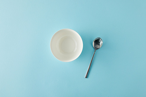 Top view of empty bowl and spoon on blue background