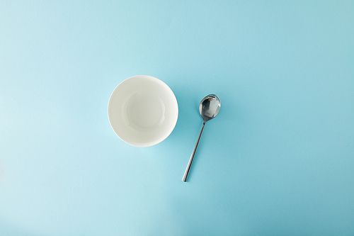 Top view of empty bowl and teaspoon on blue background
