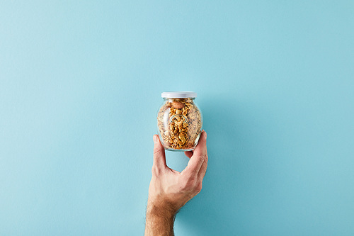 Cropped view of man holding jar of granola on blue background