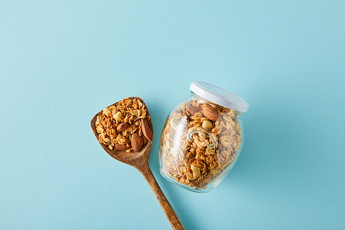 Top view of jar of granola with wooden spatula on blue background