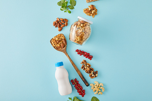 Top view of food composition of nuts, bottle of yogurt, berries and leaves of mint on blue background