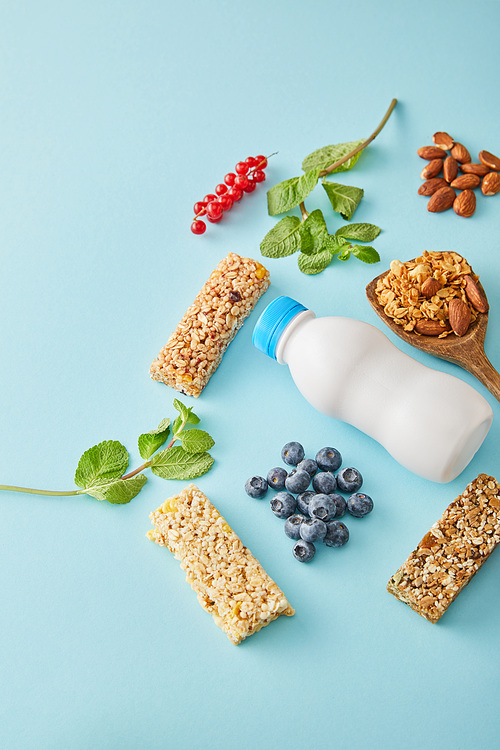 Bottle of yogurt, berries, cereal bars, mint and almonds on blue background