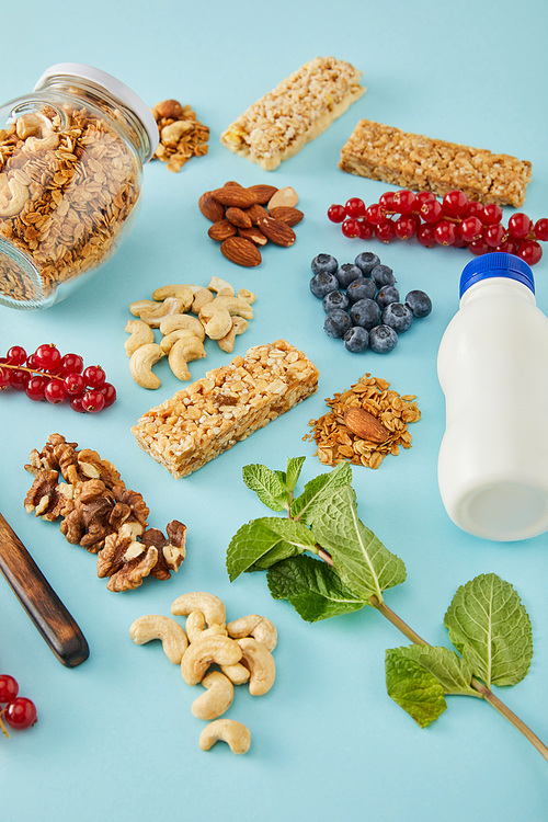 Bottle of yogurt, berries, mint, jar of granola and nuts on blue background
