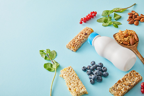Bottle of yogurt, berries, cereal bars, leaves of mint and almonds on blue background