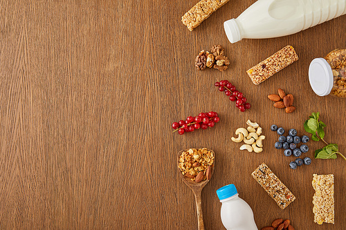 Top view of berries, nuts, cereal bars and bottles of yogurt and milk on wooden background